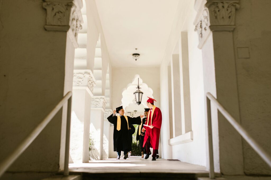 Graduates walking joyfully in academic gowns through university colonnade after ceremony.
